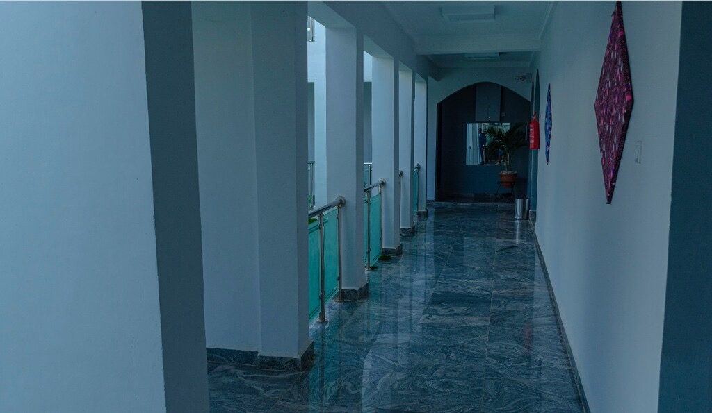 A corridor at House 7, hung with framed cloth, looking towards an arched doorway.